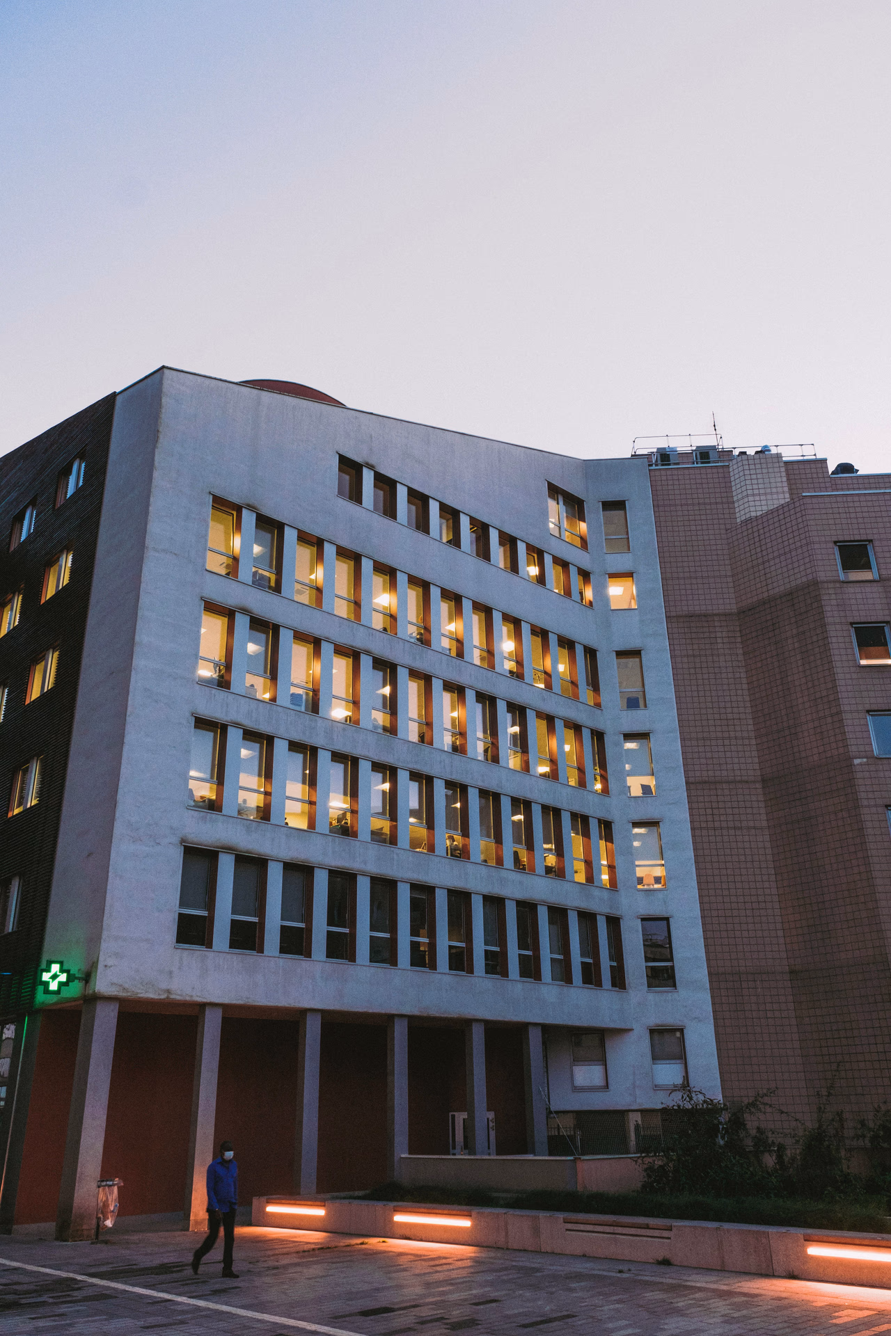 A hospital building at dusk with its windows lit from inside